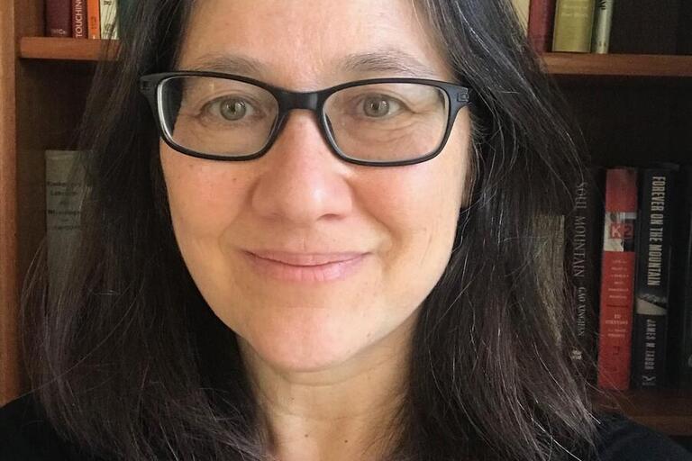 Leti standing in front of books, medium length hair and wearing glasses